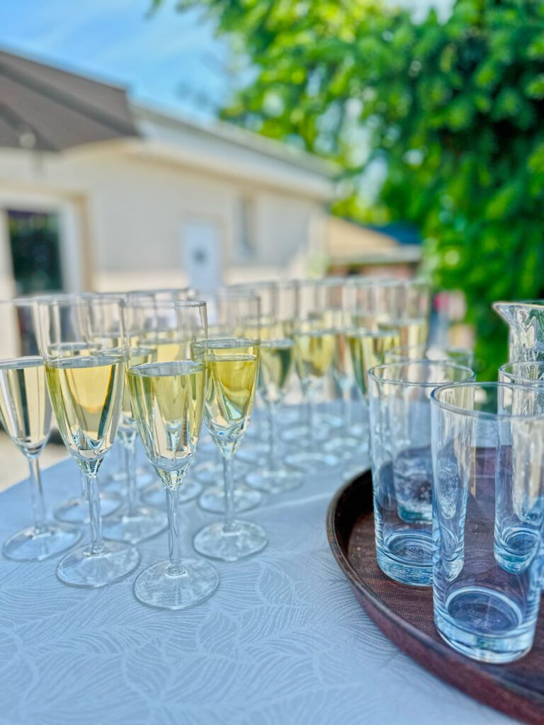 City Club & Garden: Uvítací drink pre hostí v podobe elegantných pohárov na stopke naplnených sektom, ktoré sú zoradené na stole s bielym vzorovaným obrusom.